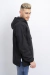 Anorak rompevientos negro visto de perfil, con capucha y bolsillo frontal.