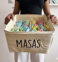 Contenedor rectangular de tela color CRUDO con la palabra "MASAS" impresa, lleno de frascos de masa para modelar y moldes de plástico de colores pastel para organizar espacios infantiles