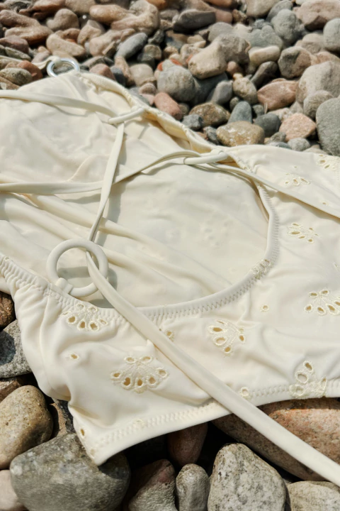Enteriza Polly Tropea off white con detalles calados y argollas, apoyada sobre piedras naturales.