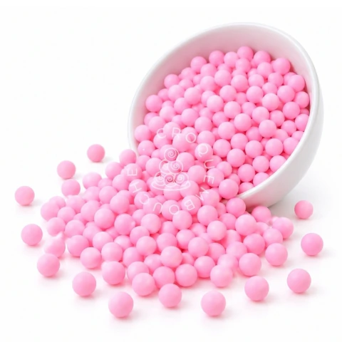 Perlas de sprinkles rosa de 8 mm esparcidas desde un bol blanco sobre una superficie blanca