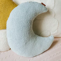 Almofada decorativa Rian Tricot Bouclé em formato de lua, na cor azul claro, sobre superfície têxtil.