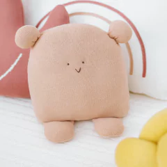 Almofada Tricô Bredy em formato de bichinho bege, com orelhas e pés, ideal para decoração de quarto de bebê e enxoval.