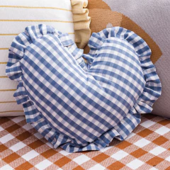 Almofada em formato de coração com estampa vichy azul e branca, acabamento com babados, ideal para decoração de quartos infantis ou enxoval de bebê.