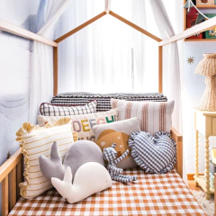 Almofadão de Encosto Vichy em um quarto infantil decorado com diversas almofadas coloridas e lúdicas sobre uma cama com tecido xadrez.