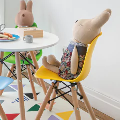 Cadeira Eames Junior amarela com base de madeira natural ao lado de mesa infantil, decorada com brinquedos e ambiente colorido.