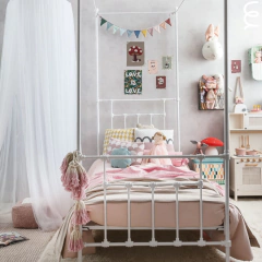 Cama de ferro solteiro estilo Versailles com dossel branca, decorada com almofadas coloridas e brinquedos em um quarto infantil aconchegante.
