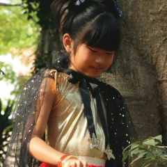Menina vestindo collant metalizado dourado da Minibossa com capa preta de tule decorada com estrelas douradas, fantasia infantil para carnaval ou festas temáticas.