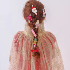 Criança vestindo a Capa Tule Esplendor Ouro da Minibossa, com detalhes dourados brilhantes, vista de costas. O cabelo está trançado e decorado com presilhas temáticas de Natal.