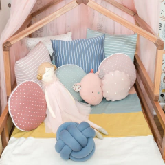 Boneca de pano Miss Carmen da Sam&amp;Peas em uma cama infantil decorada com almofadas coloridas e lúdicas.