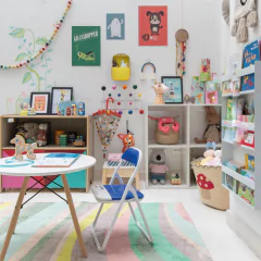 Guarda-chuva infantil Djeco com estampa colorida, exposto em um quarto infantil decorado com brinquedos, livros e móveis lúdicos.
