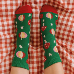 Meia 3/4 infantil verde com estampa de bolas de Natal, estrelas e toques vermelhos da marca Cantarola, sobre um tecido xadrez vermelho e branco.