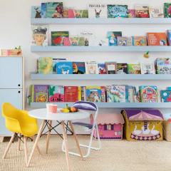 Mesa Eames Junior branca com base de madeira natural em ambiente infantil, acompanhada de cadeiras coloridas e estante de livros ao fundo.