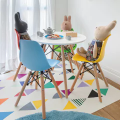 Mesa Eames Junior branca com base de madeira natural, acompanhada de cadeiras coloridas infantis e bonecos de pelúcia, em ambiente decorado para crianças.