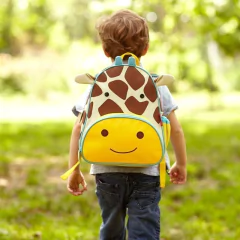 Mochila infantil Skip Hop Zoo modelo girafa, com detalhes amarelos, marrom e branco, pendurada em cabideiro escolar.