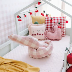 Protetor de berço em formato de crocodilo com estampa xadrez rosa e branco, ideal para decoração de quarto de bebê.