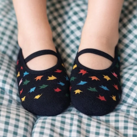 Sapatilha infantil preta com estampa de dinossauros coloridos da marca Cantarola, modelo Pegada Dino, nos pés de uma criança.