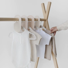 Set de cabides de veludo off-white da marca 3 Sprouts organizando roupas infantis em um cabideiro de madeira.