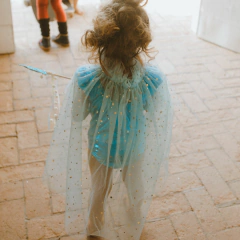 Criança vestindo a Capa Céu de Estrelas Azul da Minibossa, com tule azul e detalhes de estrelas douradas, vista de costas.