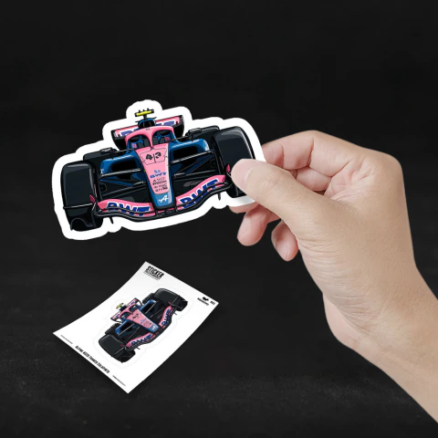 Mano sosteniendo un sticker del auto de Fórmula 1 Alpine 2026 de Franco Colapinto en colores rosa y azul