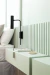 Aplique de pared Cavia de brazo corto instalado junto a una cama con almohadas y una mesita de noche de color verde claro.