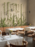 Aplique de pared Cavia - Brazo Largo instalado en un restaurante con plantas verdes en la pared.