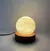 Velador de mesa con base redonda de madera y esfera luminosa, ideal para decorar espacios.