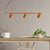 Colgante de tres luces modelo Teo Linear, color terracota, instalado sobre una mesa de madera con una planta decorativa y una taza blanca.