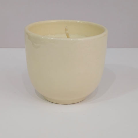 Vela blanca en un cuenco de cerámica liso color crema sobre superficie blanca
