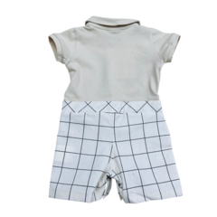 Macacão infantil com parte superior bege e calças brancas com estampa de quadrados pretos.