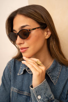 Primer plano de mujer con gafas de sol MIU Eclipta de montura oscura y diseño ovalado, vestida con chaqueta de jean y anillo dorado en forma de flor