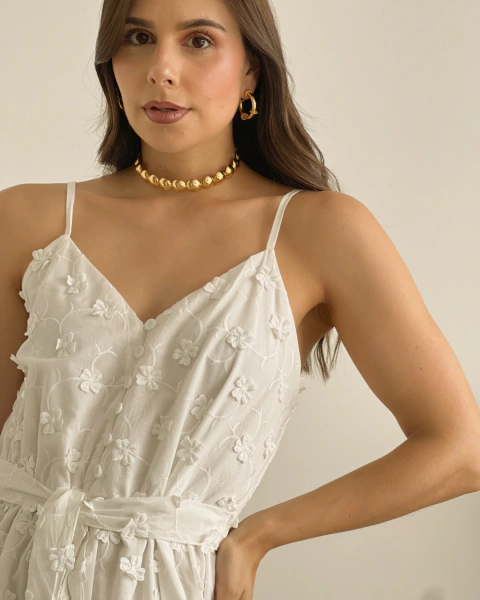 Detalle frontal del vestido blanco T.156 de PRIMIA, con escote en V, tirantes delgados, botones blancos, flores bordadas en relieve y cinturón anudado.