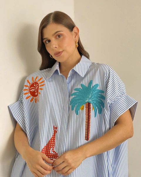 Detalle frontal del vestido P.080 de PRIMIA, mostrando el cuello camisero, las rayas verticales y las aplicaciones de sol naranja, palmera turquesa y figura roja.