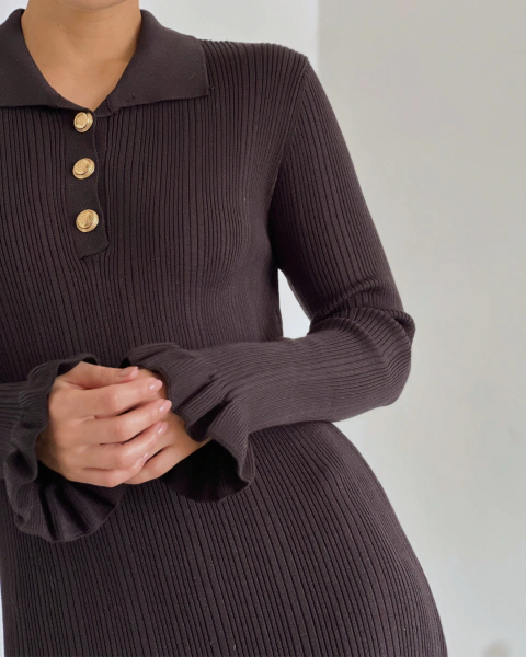 Detalle frontal del vestido T.202 negro de PRIMIA con textura acanalada, botones dorados y puños acampanados con volantes.