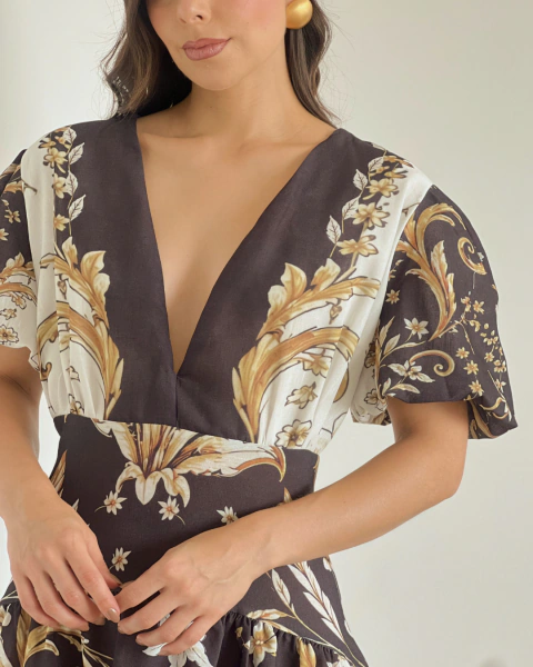 Vestido T.146 de PRIMIA, primer plano del escote en V, las mangas amplias, el panel de cintura y los motivos florales dorados sobre fondo café oscuro y marfil.