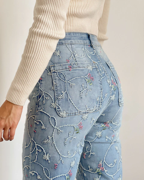 Jean NOHELA Azul de PRIMIA, detalle posterior de la cadera con bolsillos de parche y bordados de ramas entrelazadas, pequeñas flores rosadas y hojas verdes.