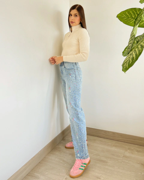 Jean NOHELA Azul de PRIMIA, vista lateral de cuerpo completo con bordados florales a lo largo de las piernas, cintura alta y ruedo recto.