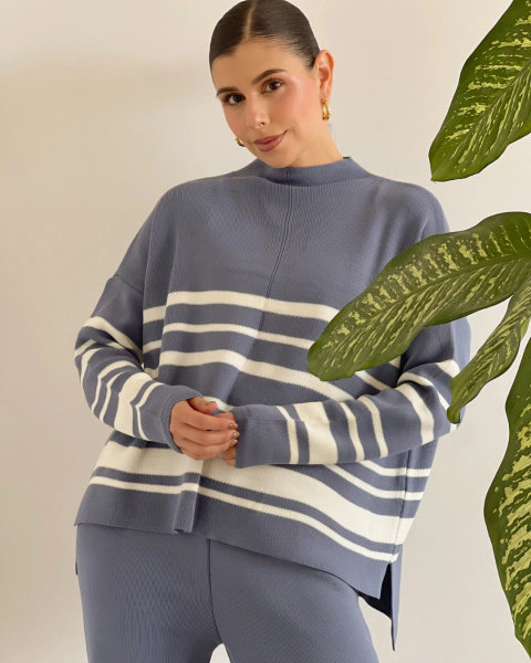 Conjunto azul de PRIMIA, primer plano frontal del buzo de cuello alto con textura de punto, rayas blancas horizontales y mangas amplias.
