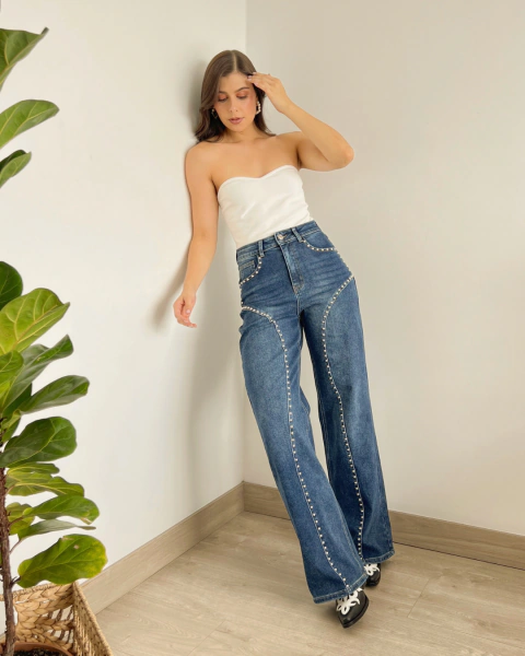Jean de mujer P.096 de PRIMIA, vista frontal de cuerpo completo con denim azul de efecto lavado, pierna amplia y aplicaciones metálicas.