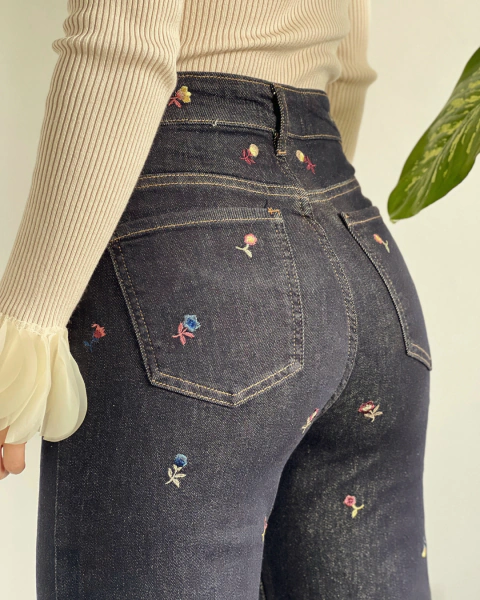 Detalle posterior del Jean SERPENTINA de PRIMIA, con bolsillos de parche y flores multicolor bordadas sobre denim azul oscuro.