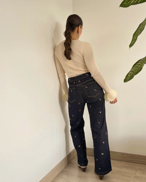 Jean SERPENTINA de PRIMIA, vista posterior de cuerpo completo con tiro alto, pierna amplia y flores bordadas sobre denim azul oscuro.