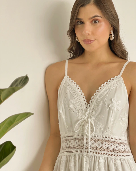 Detalle frontal del vestido blanco T.158 de PRIMIA, con escote profundo en V, terminaciones de encaje, lazo de cordón y cintura calada.