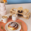 Conjunto de potes de vidro com tampa de bambu para temperos, acompanhado de café e um pão doce em uma mesa decorada.