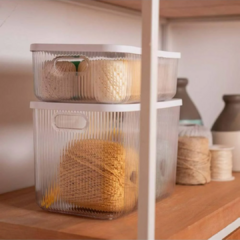 Caixas organizadoras caneladas transparentes com tampa, empilhadas e contendo materiais de artesanato, em uma prateleira de madeira.