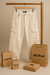 Pantalón cargo beige de la marca VACKUA, exhibido en un perchero junto a varias bolsas de papel con el logo de la marca.