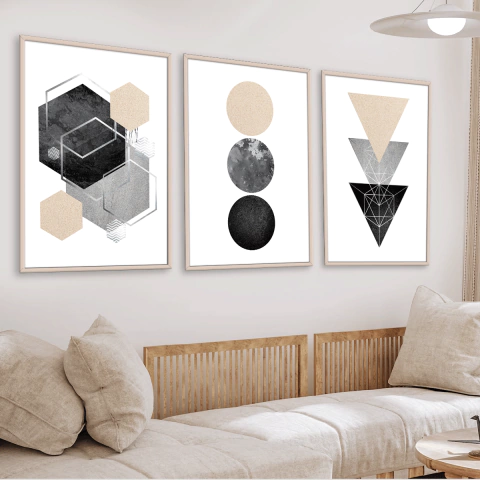 Set de 3 cuadros beige con diseños geométricos en tonos negros, grises y beige, colgados sobre un sofá claro en un living moderno