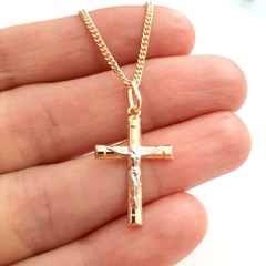 Colar folheado a ouro com cruz e Cristo, segurado por uma mão.
