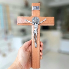 Cruz de madeira imbuia com figura de Cristo em metal, segurada por uma mão