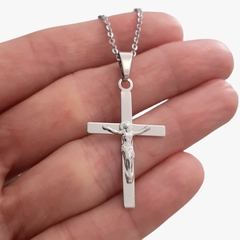 Colar de aço com pingente de cruz e figura de Cristo, segurado na mão.