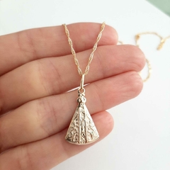 Colar folheado a ouro com pingente de Nossa Senhora Aparecida em uma mão.