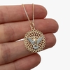 Colar folheado a ouro com pingente de mandala e figura de um espírito santo em destaque, segurado por uma mão.
